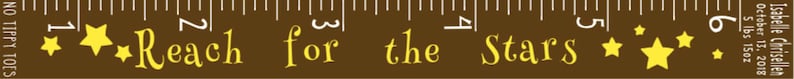 May include: A brown growth chart ruler with white markings and the text "Reach for the Stars" in a decorative font. Yellow stars are scattered across the ruler. The ruler measures up to 6 inches.