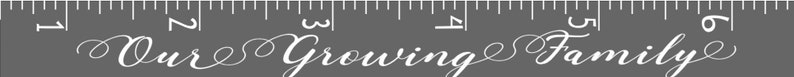 May include: A gray background with a white ruler and the words "Our Growing Family" in elegant script. The ruler is marked with white lines and numbers, suggesting a measurement tool or growth chart.