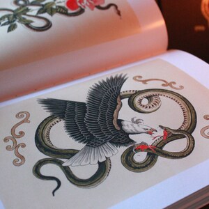 May include: A black and white eagle with its wings spread, attacking a green snake with its beak. The snake is coiled around the eagle's body. The image is surrounded by decorative swirls in a light brown color.