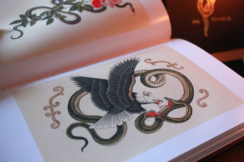 May include: A black and white eagle with its wings spread, attacking a green snake with its beak. The snake is coiled around the eagle's body. The image is surrounded by decorative swirls in a light brown color.