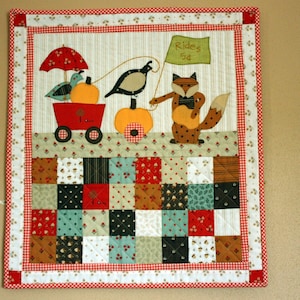 May include: A colorful patchwork quilt with a whimsical scene of a fox, a bird, and a pumpkin cart. The quilt features a red and white gingham border and the text "Rides 5c".