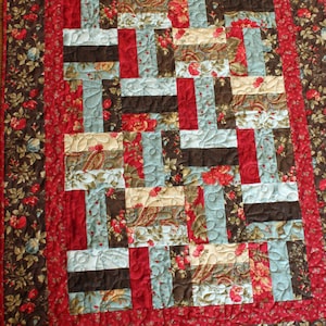 May include: A quilt with a patchwork design featuring various floral patterns in shades of red, brown, blue, and cream. The quilt is quilted with a swirling pattern.