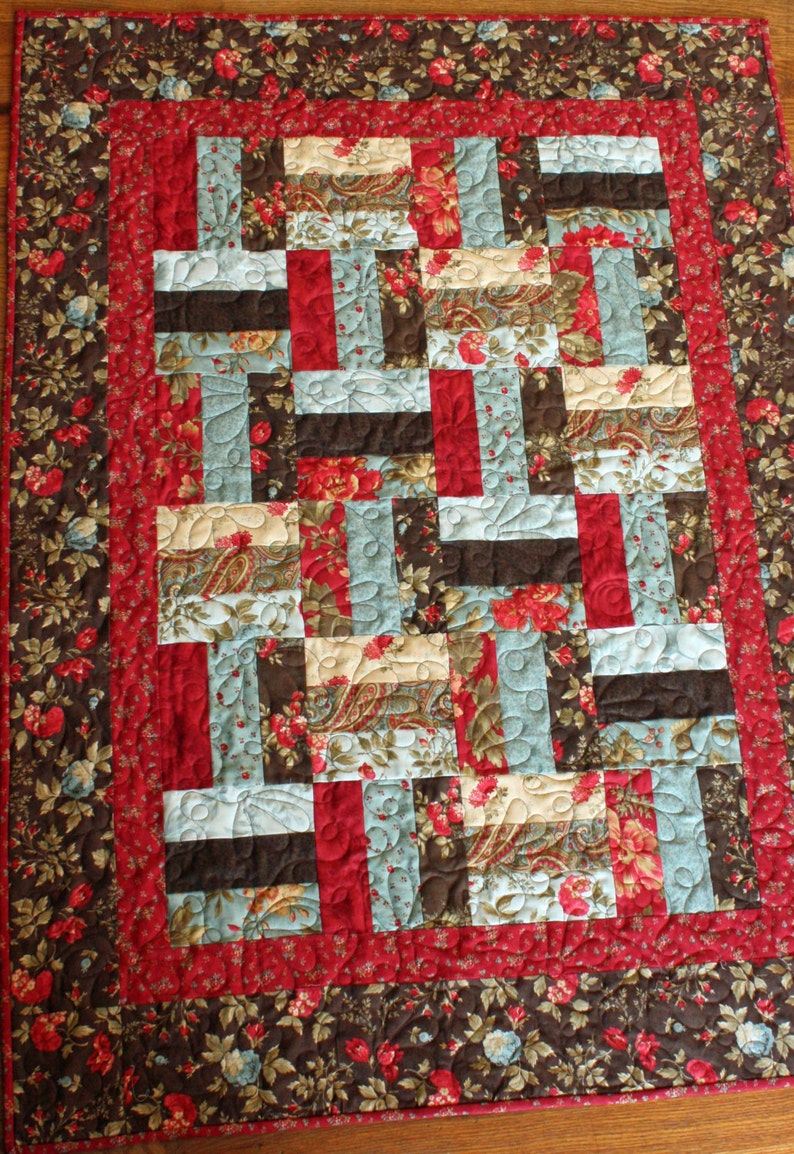 May include: A quilt with a patchwork design featuring various floral patterns in shades of red, brown, blue, and cream. The quilt is quilted with a swirling pattern.