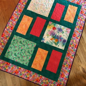 May include: A patchwork quilt with a green background and various colorful floral patterns. The quilt is made up of nine squares, each with a different pattern. The squares are surrounded by a border of small, colorful flowers.