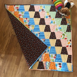 May include: A brown and white baby quilt with a geometric pattern of triangles and squares. The quilt features a variety of colors, including blue, green, yellow, orange, and red. The quilt is made of cotton fabric and is machine washable.