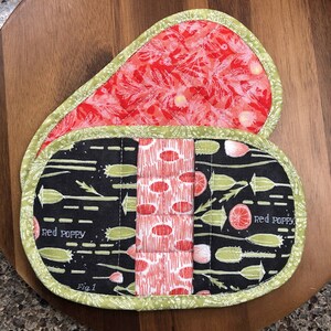 May include: Two red and black quilted pot holders with green trim. The pot holders have a floral pattern and the text "Red Poppy" is printed on them. One pot holder has the text "Fig 1" printed on it.