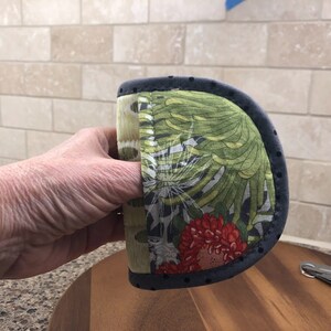May include: A green, red, and black patterned pot holder with a black polka dot trim. The pot holder has a finger loop for easy handling.