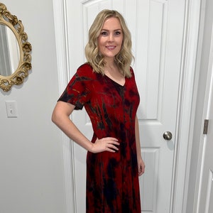 May include: A red, black, and brown tie-dye midi dress with a v-neck and short sleeves. The dress is worn with brown ankle boots.