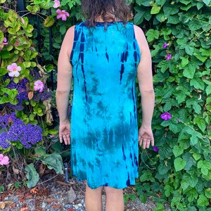 May include: A sleeveless dress with a tie-dye pattern in shades of blue and green. The dress is made of a soft, flowing fabric and has a relaxed fit.