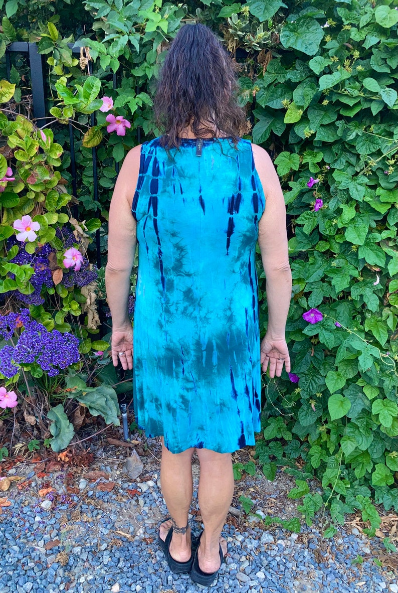 May include: A sleeveless dress with a tie-dye pattern in shades of blue and green. The dress is made of a soft, flowing fabric and has a relaxed fit.