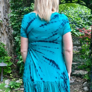 May include: A turquoise tie-dye tunic with a ruffled hem. The tunic has a scoop neck and short sleeves.