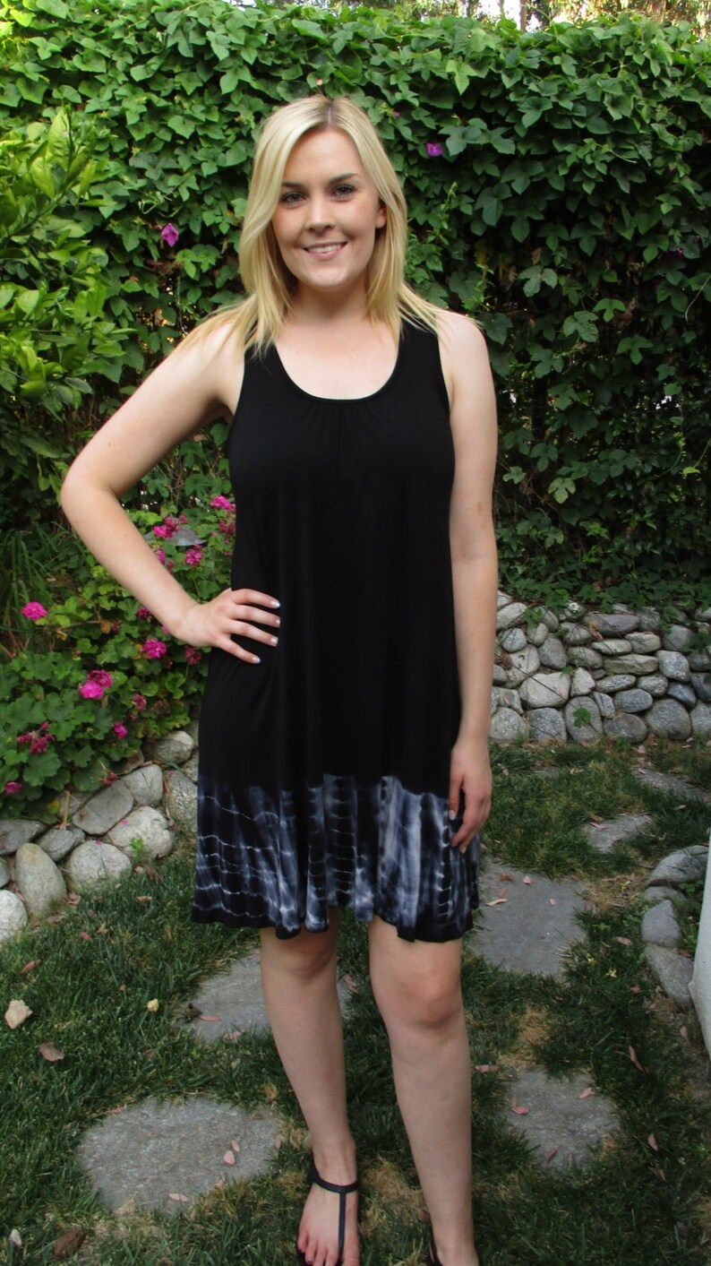 May include: A woman wearing a black sleeveless dress with a tie-dye hem. The dress has a scoop neckline and a relaxed fit.