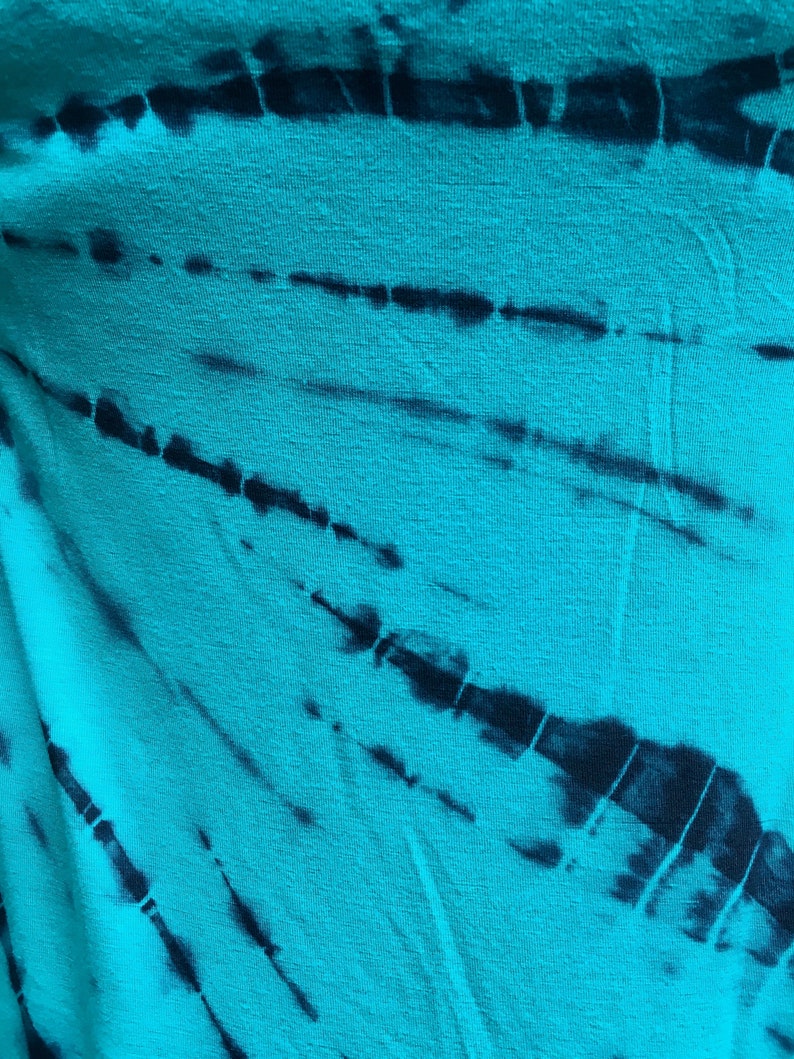 May include: A turquoise fabric with a black tie-dye pattern. The fabric has a soft, textured surface.