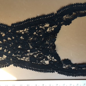 May include: Black lace trim with a scalloped edge. The trim features an openwork floral design. The lace is made of a soft, delicate material. This trim is suitable for various sewing and craft projects.