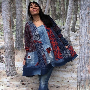 Op de afbeelding: Een vrouw draagt een blauwe, rode en witte patchwork tuniek met een distressed denim zoom. Ze staat in een bosrijke omgeving.