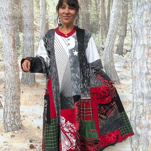 Puede incluir: Un vestido de patchwork de manga larga con una mezcla de telas negras, blancas, rojas y verdes. La prenda incluye varios patrones como cuadros, rayas e impresiones gráficas, con un cuello rojo, un cierre de un solo botón y una silueta acampanada.