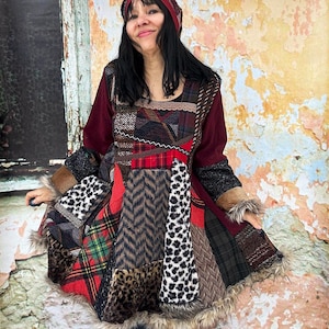 Op de afbeelding: Een patchwork jurk met verschillende patronen en texturen, waaronder ruitjes, dierenprints en visgraat. De jurk heeft een bordeauxrood lijfje en mouwen, met imitatiebont langs de manchetten en zoom. Een bijpassende bordeauxrode haarband.