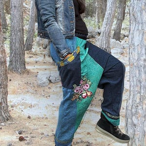 Könnte beinhalten: Jeans-Patchworkhose mit floraler Stickerei. Die Hose hat eine Mischung aus blauem Denim und grünen Stoffbahnen. Das Design umfasst eine florale Stickerei auf der Vorderseite. Getragen mit schwarzen Schuhen.