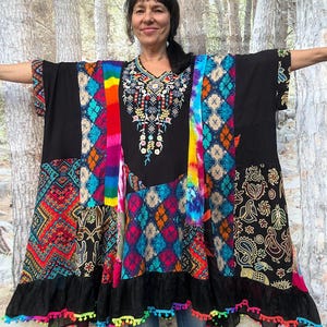 Könnte beinhalten: Eine schwarze Tunika mit V-Ausschnitt und bunter Blumenstickerei. Das Kleidungsstück besteht aus verschiedenen Patchwork-Einsätzen, darunter Batik-, geometrische und Stammesmuster in leuchtenden Farben. Der Saum ist mit einer schwarzen Rüsche versehen.
