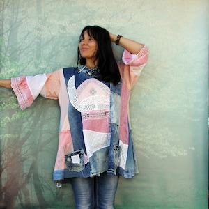 May include: A woman wearing a denim and lace patchwork tunic with a pink and white design. She is wearing blue jeans and has her hair pulled back.