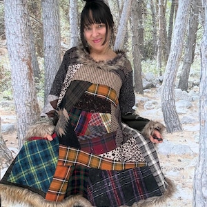 Op de afbeelding: Een patchworkjas met verschillende ruitpatronen in groen, oranje, rood en zwart. De jas heeft een imitatiebontrand rond de kraag en zoom. De mouwen zijn van donkergrijs gebreid materiaal.