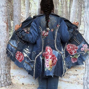 Può includere: Una giacca in denim blu scuro caratterizzata da un design patchwork con bordi sfrangiati, sezioni consumate e ricami floreali in tonalità di rosso, rosa e giallo. La giacca presenta tasche multiple e dettagli di cucitura elaborati.