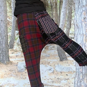 May include: Plaid drop-crotch pants in shades of red, brown, and black. The pants feature a patchwork design with various plaid patterns and a relaxed fit. The model is wearing a black jacket and black boots.