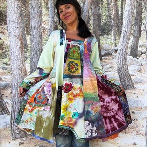 Könnte beinhalten: Eine langärmelige Tunika mit Patchwork-Design, bestehend aus verschiedenen Blumenmustern, Batik-Mustern und einfarbigen hellgrünen Stoffbahnen. Das Kleidungsstück hat eine ausgestellte Silhouette, einen eckigen Ausschnitt und sichtbare Nähte.