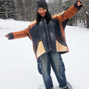 Puede incluir: Una chaqueta patchwork en tonos marrón, beige y mezclilla azul, con cremallera completa. La chaqueta se combina con pantalones cargo de mezclilla azul. Un gorro gris oscuro completa el atuendo. La persona está de pie en la nieve.