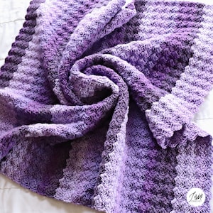 May include: A purple and lavender ombre crochet baby blanket with a scalloped edge.