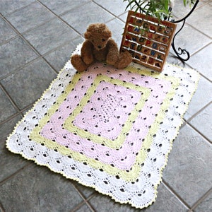 May include: A crocheted baby blanket with a white, yellow, and pink color scheme. The blanket has a scalloped edge and a square design in the center.