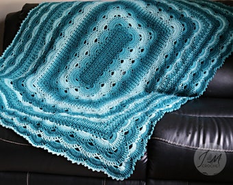 May include: A teal and aqua crochet blanket with a scalloped edge. The blanket is draped over a black leather couch.