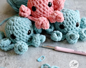 May include: Three handmade crochet octopuses in shades of pink and blue. The octopuses have black button eyes and curled tentacles. A crochet hook, stitch marker, and yarn are also visible.