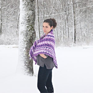 May include: A person is wearing a purple and white crocheted shawl in a snowy outdoor scene. The shawl has a scalloped edge and a striped pattern in shades of purple and white. The person is wearing a grey shirt and black trousers.
