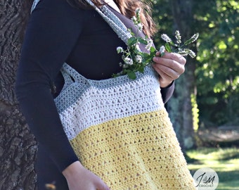 May include: A crocheted tote bag with a gray, white, and yellow striped design. The bag has a wide, open top and two long straps. The bag is being held by a person in a black shirt.