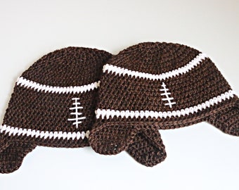 May include: Two brown crocheted hats shaped like footballs with white stripes and stitching details.