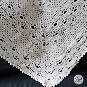 May include: An off-white crochet blanket featuring a repeating fan-shaped stitch pattern with openwork details. The bottom right corner displays a circular logo with the text JM CROCHET and a small butterfly icon.