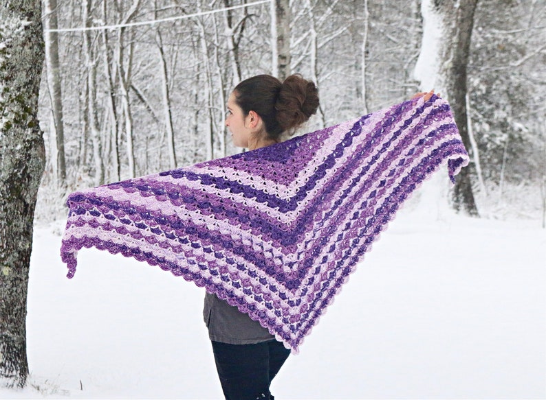 May include: A handmade, purple and white crochet shawl. The shawl is a V-shape, with alternating stripes of light and dark purple. The background is a snowy forest scene.