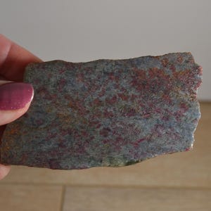 May include: A close-up of a piece of polished stone with a mottled pattern of gray, pink, and brown. The stone has a rough, irregular edge.