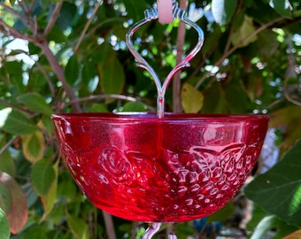 May include: A red glass hummingbird feeder with a decorative grape design hangs from a silver hook.