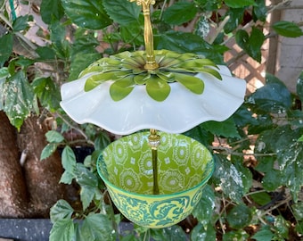 May include: A two-tiered decorative stand featuring a white ruffled ceramic plate on top, topped with a green metal flower accent, and a green and white patterned ceramic bowl on the bottom, connected by a central gold-toned metal rod handle.