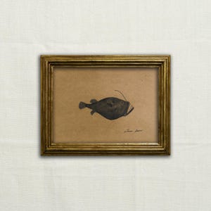 Könnte beinhalten: Eine gerahmte Schwarzweißzeichnung eines Tiefsee-Anglerfisches mit einem langen, dünnen Filament, das sich von seinem Kopf erstreckt. Die Zeichnung befindet sich auf einem braunen Papierhintergrund und ist mit "Simon Fraser" signiert.