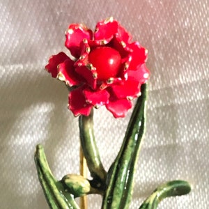 May include: A red flower with gold accents in a black pot. The flower has green leaves and a gold stem.