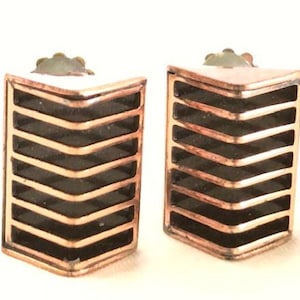 May include: A pair of copper earrings with a geometric chevron design. The earrings are black and copper in colour.