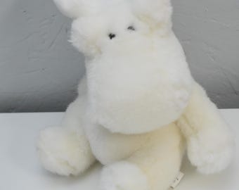 May include: A plush stuffed animal in the shape of a moose, covered in soft, off-white fur. The toy features large, upright antlers, a rounded snout, and small, dark, bead-like eyes. It is depicted in a seated position with visible limbs.