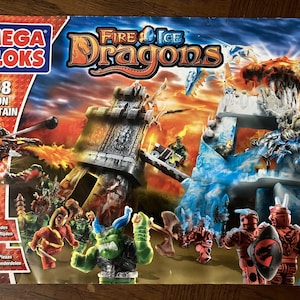 May include: Mega Bloks Fire & Ice Dragons Dragon Mountain playset box. The box features a fantasy scene with dragons, warriors, and a fortress. The box includes the text "9858 Dragon Mountain" and "255 Pieces".