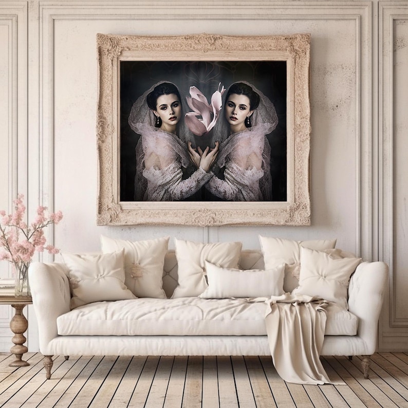 May include: A framed artwork featuring two women in vintage attire, holding a pink flower. The artwork is displayed above a cream-colored sofa with pillows and a throw. The room has a neutral color palette with wooden floors.