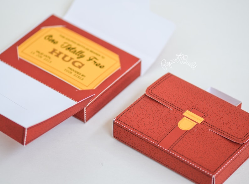 May include: A red cardboard box with a yellow label that says "One Totally Free HUG" and a red leather-like box with a gold buckle.