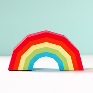 Puede incluir: Una manualidad de arcoíris de papel de colores con rayas rojas, naranjas, amarillas, verdes, azules y moradas. El arcoíris está hecho de papel doblado y tiene una forma tridimensional.