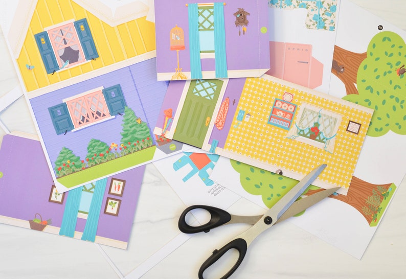 May include: A set of colorful paper cutouts for a paper dollhouse, including a yellow house with blue shutters, a purple room with blue curtains, a green door, a yellow room with a window, and two green trees. The cutouts are on a white surface with a pair of silver scissors.
